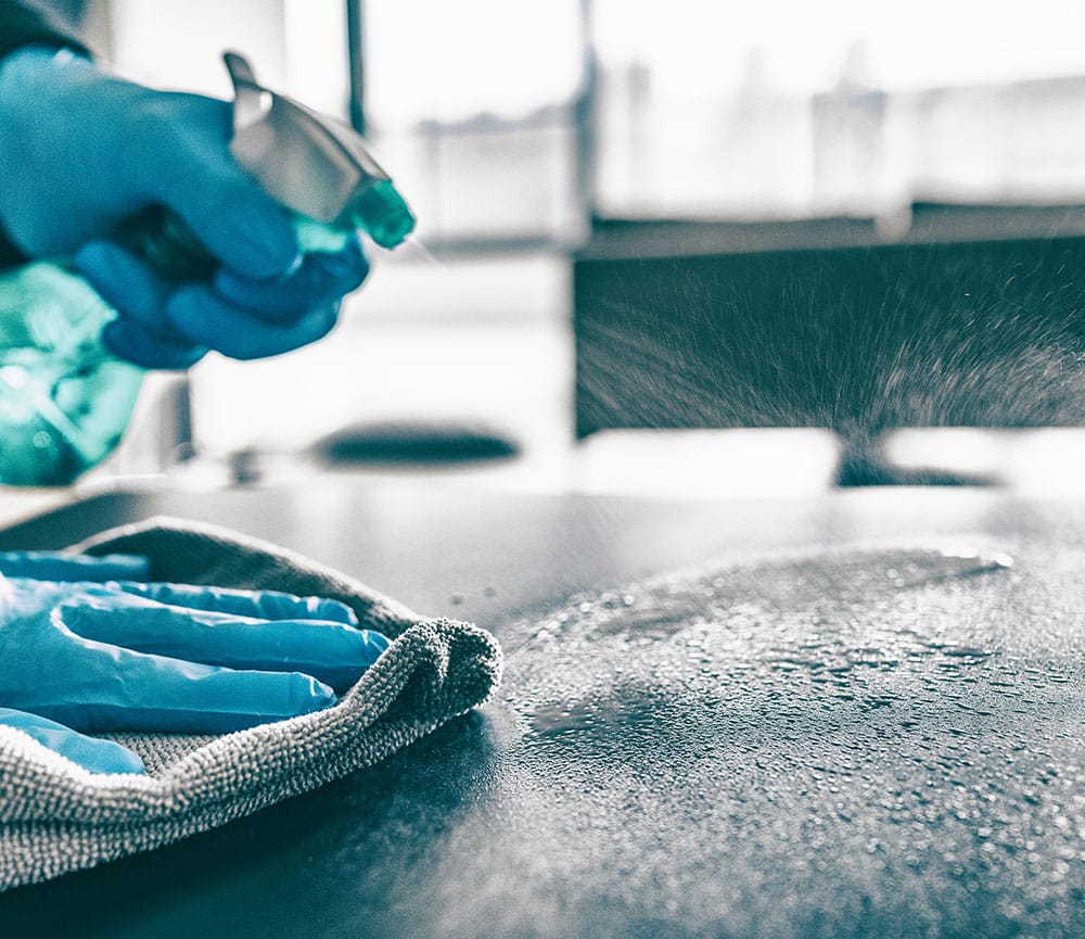A gloved hand wiping down a surface with cleaning spray